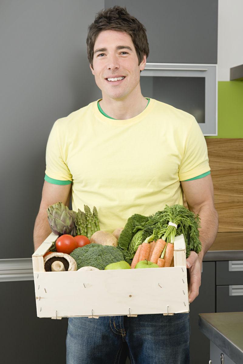 厨房里男人端着装满蔬菜的箱子