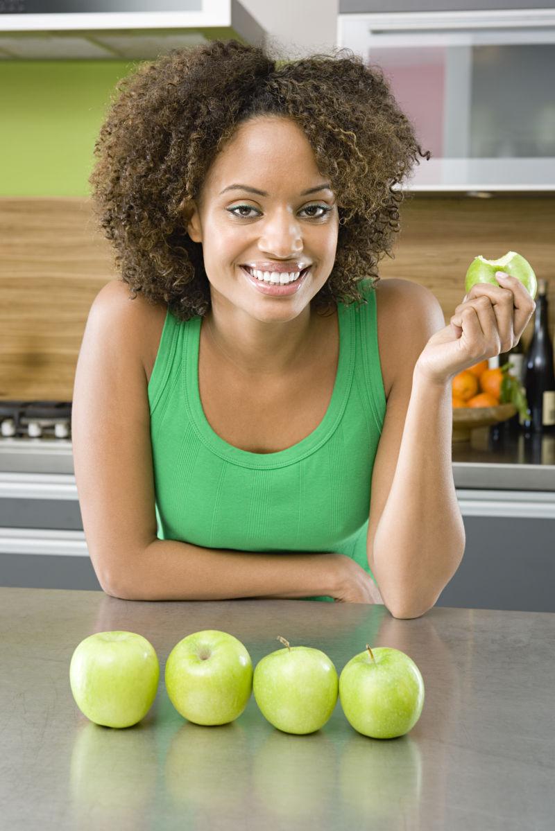 厨房里的非洲女人拿着一个苹果和桌面上四个青苹果