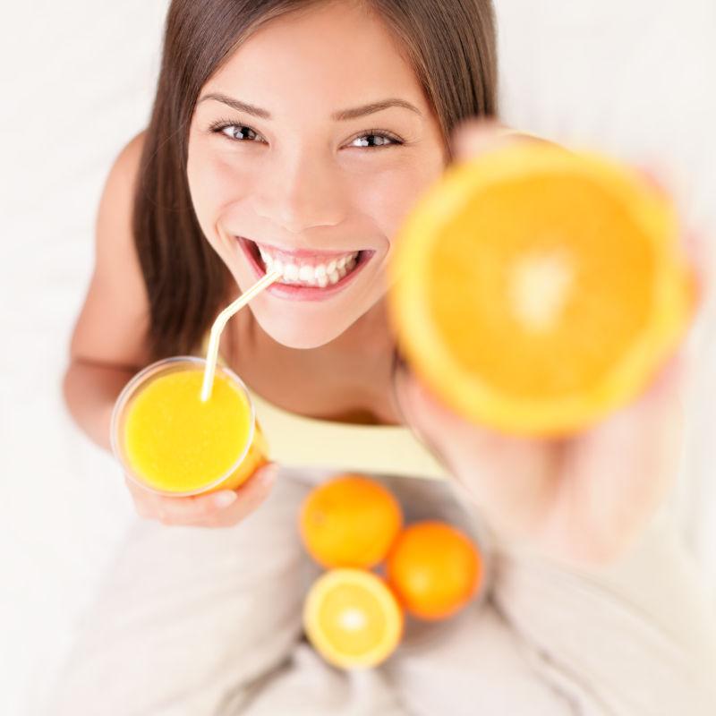 女孩喝着新鲜的橙汁手里拿着橙子