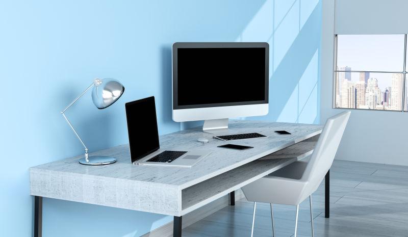 在蓝色墙旁边办公桌上的笔记本电脑等办公设备