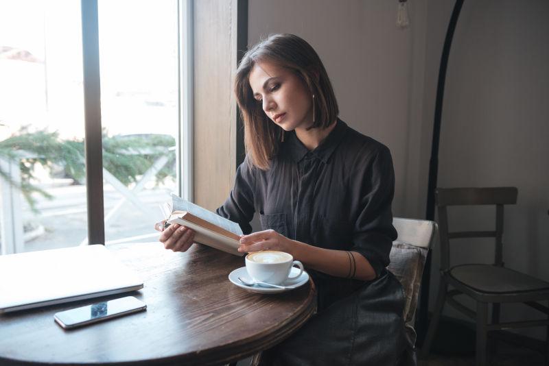一张年轻漂亮的女人坐在咖啡桌旁看书