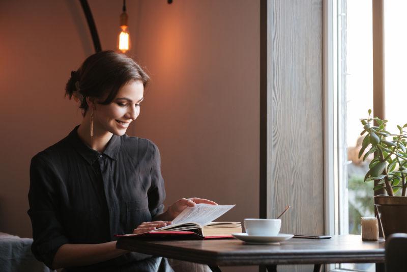 微笑的年轻女子在咖啡馆边喝咖啡边看书