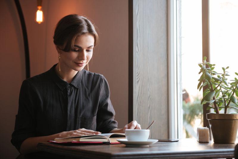 一位年轻漂亮的女士在咖啡店一边喝咖啡一边看书