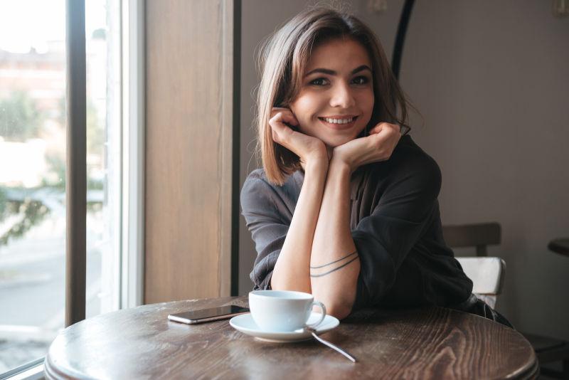迷人的年轻女士坐在咖啡桌旁喝咖啡