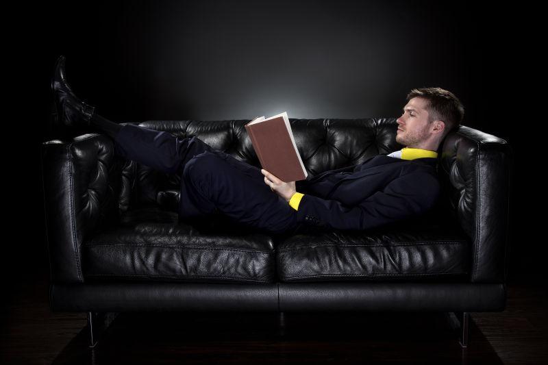 黑色背景下躺在沙发上看书的男人