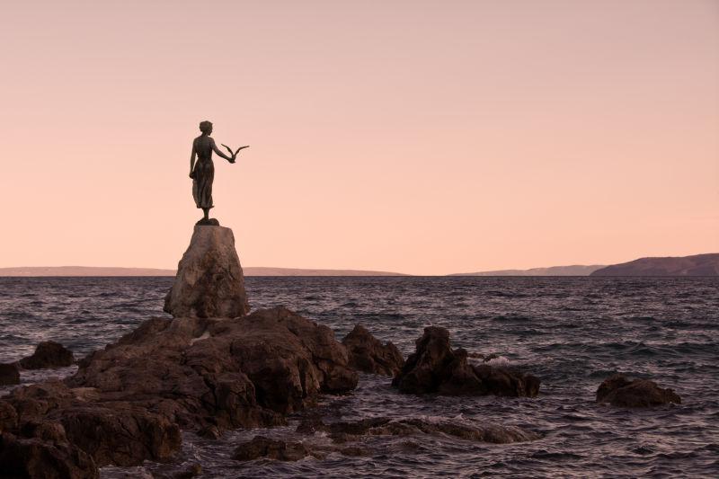 夕阳下立在岩石上的少女雕像