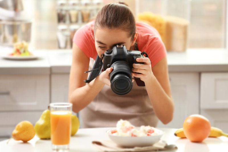 厨房背景中拿着相机拍摄美食的女人