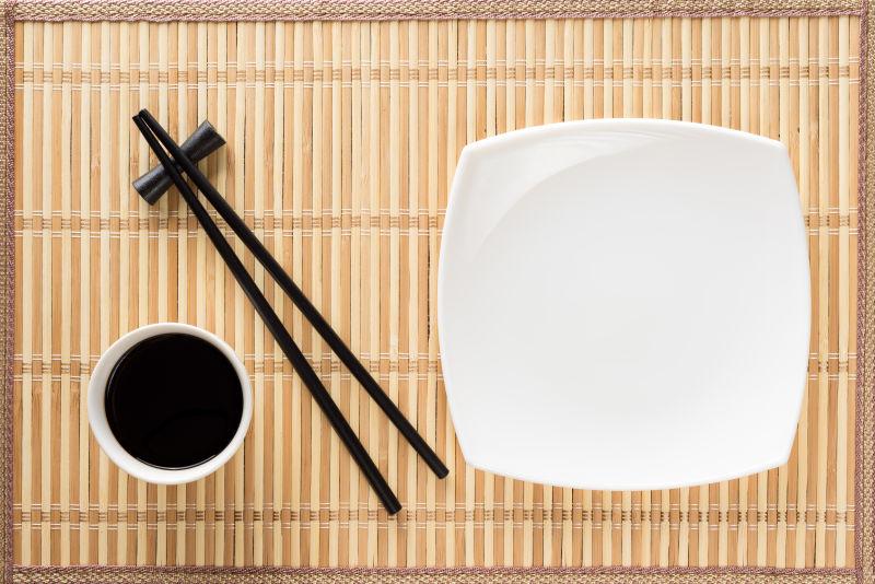 竹席上的方形盘子和酱油碗还有一双黑色筷子
