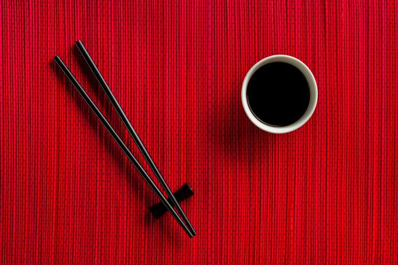 红色竹席桌面上的酱油碗和黑色筷子