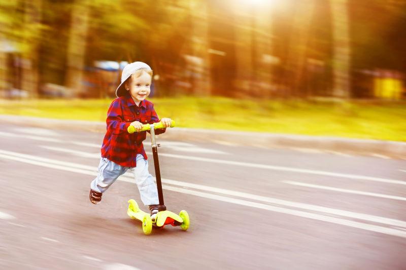 戴帽子的小男孩在夏日公园里快乐地骑滑板车
