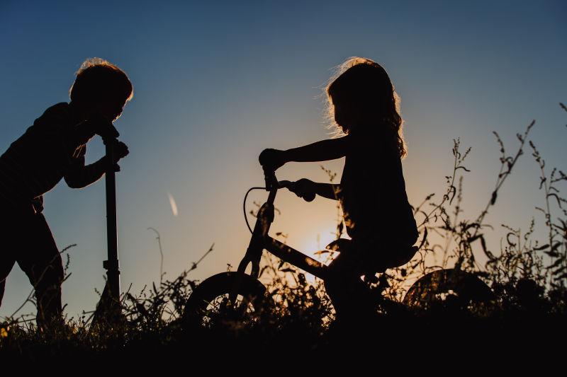日落时骑自行车和滑板车的孩子