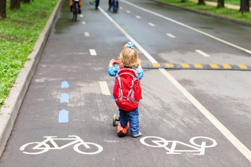 可爱的小蹒跚学步的女孩在城市骑着踏板车