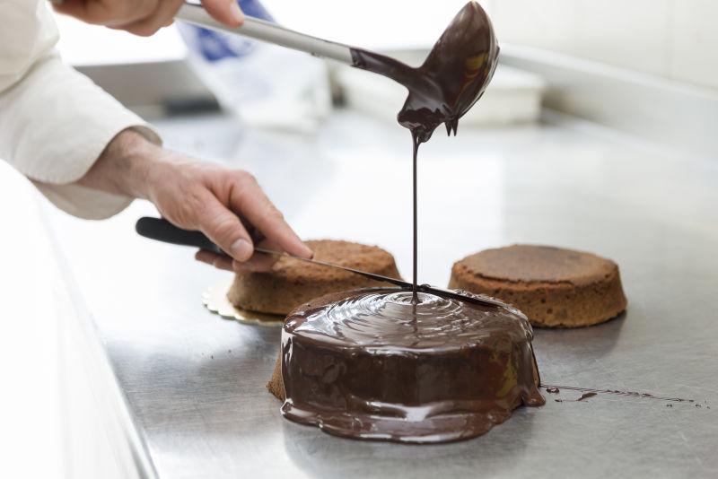 糕点厨师用融化巧克力覆盖蛋糕