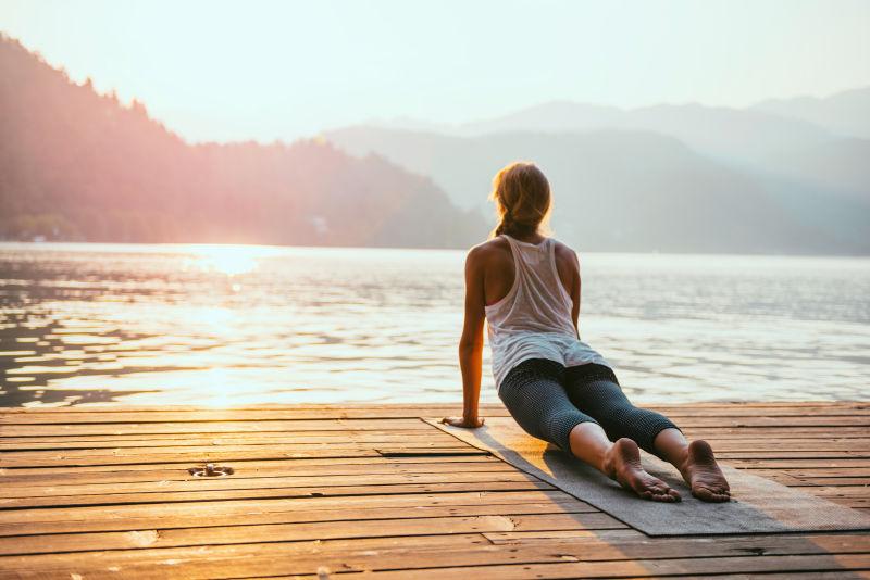 美丽的女人在湖边练习瑜伽向着太阳致敬