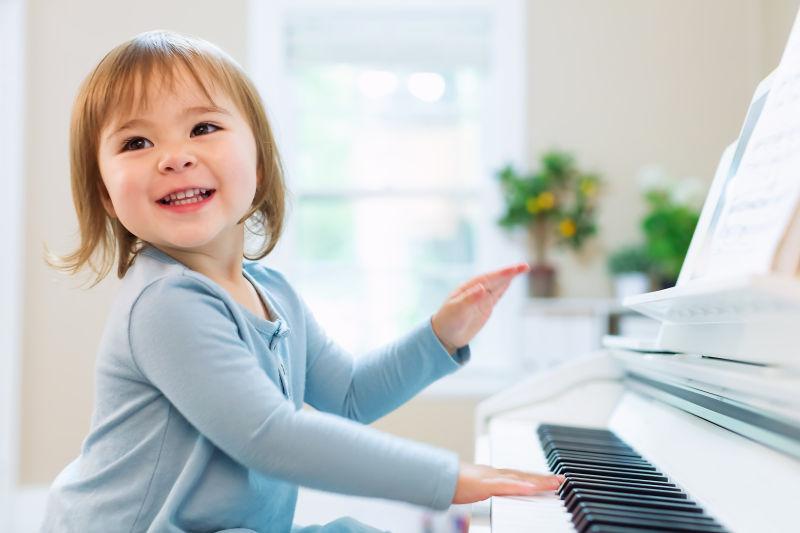 快乐的微笑的幼儿女孩弹钢琴