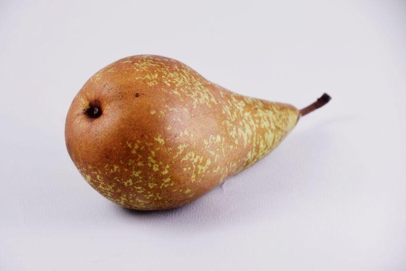 躺在白色桌上的一只褐色的梨子
