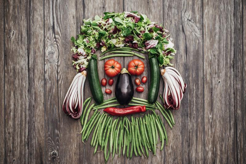 微笑的人用新鲜的五颜六色的蔬菜在质朴的木质台面制成的胡须脸