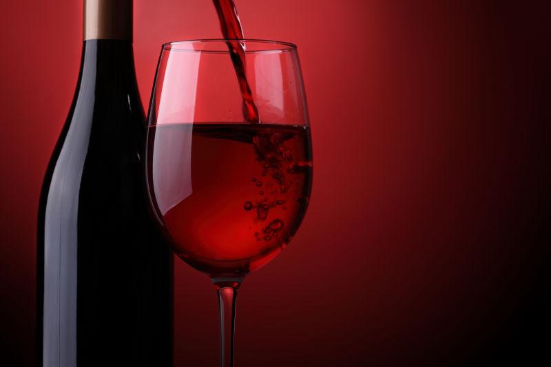 暗红色背景下倒入高脚杯的红酒和红酒瓶