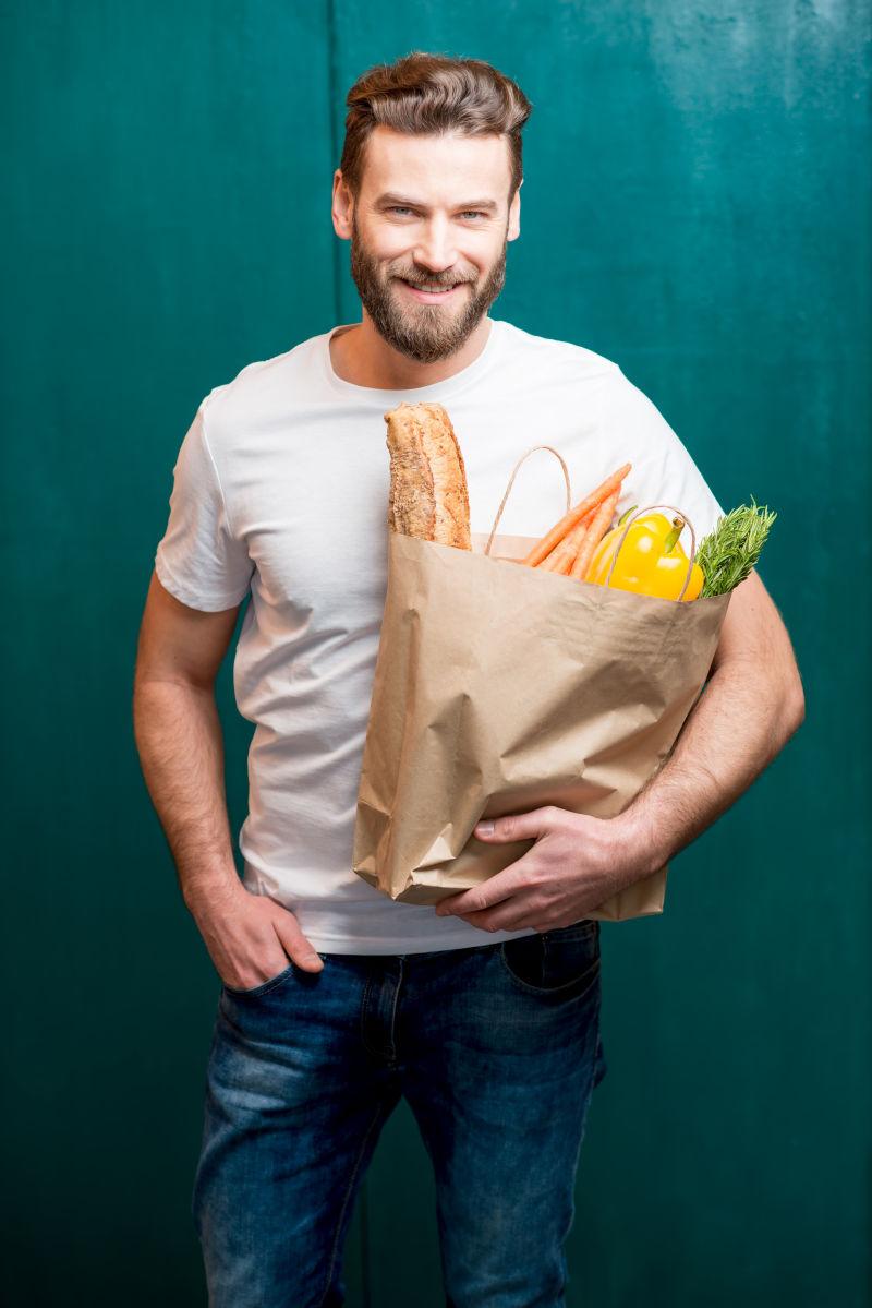 在绿色背景下拿着一袋装满健康食品的帅哥