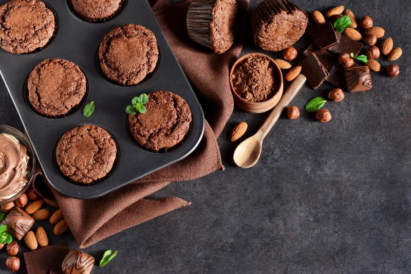 黑色背景下的褐色亚麻布上的巧克力松饼和坚果