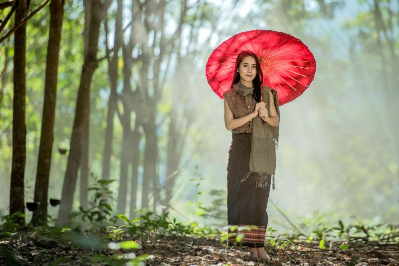 在树林中撑着红色伞的年轻美女