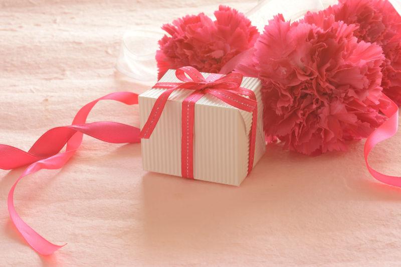 粉色背景上的粉红色康乃馨和礼品盒