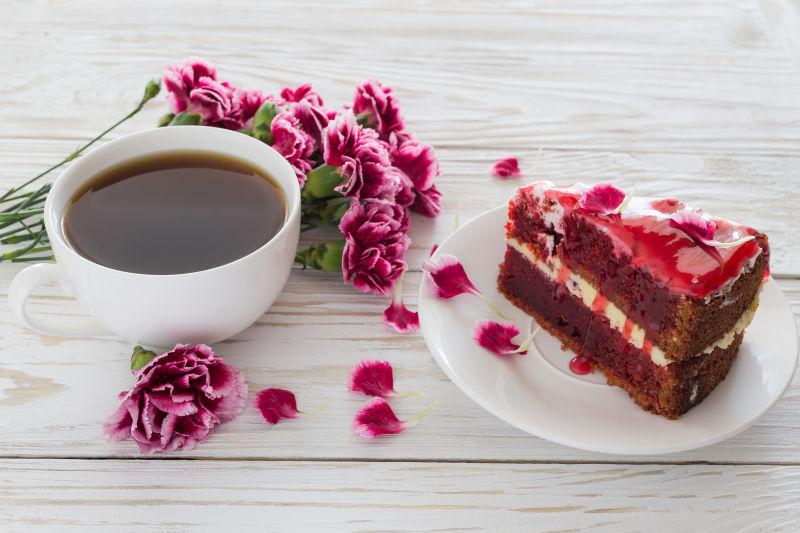 白色木桌上的粉红康乃馨和一块红色的蛋糕