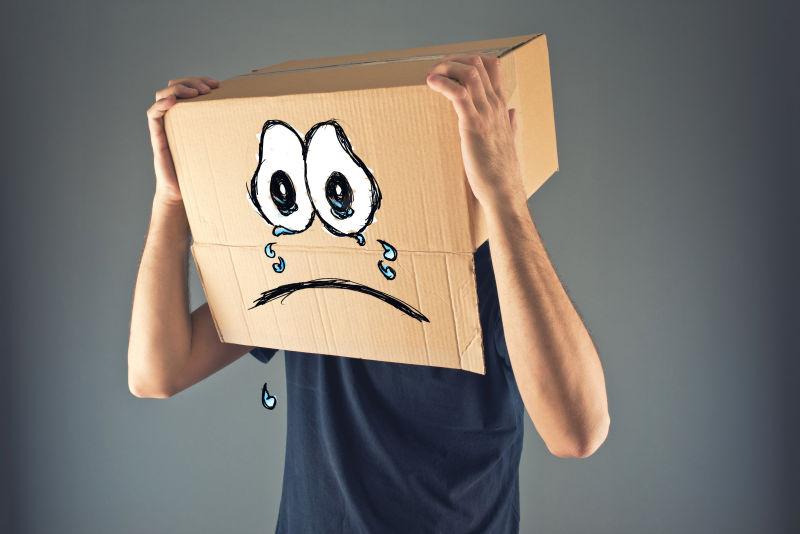 男人用画着哭脸表情的纸箱放在头上