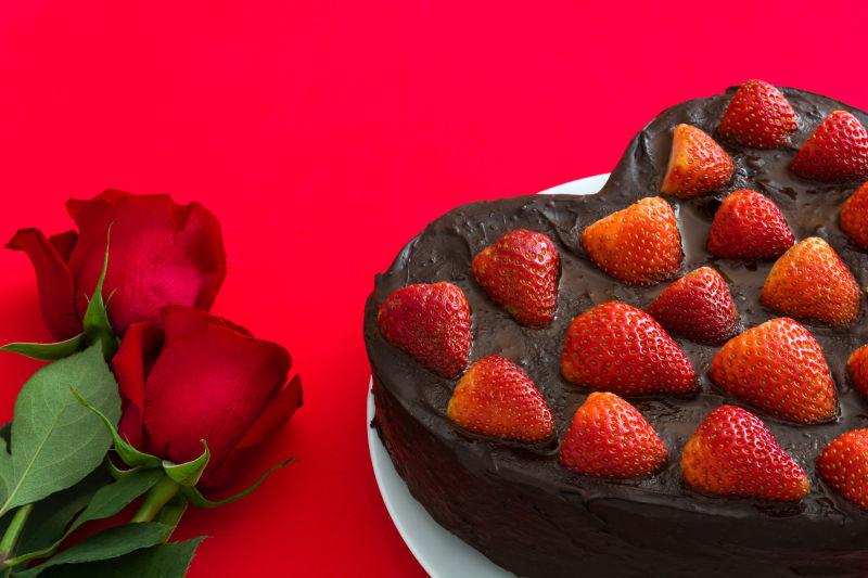 红色桌面上的草莓蛋糕和玫瑰花