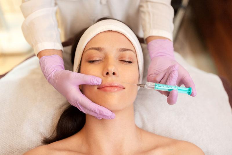 美容师用注射器做透明质酸注射增强年轻女性嘴唇