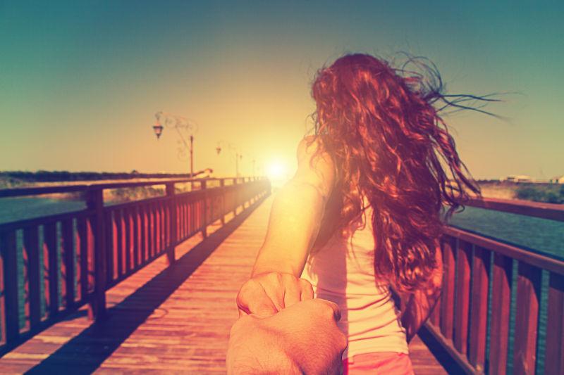 阳光下海滩桥上女子拉着男友的手