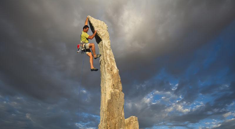 男性攀岩者从一个纯粹的岩石尖顶悬垂
