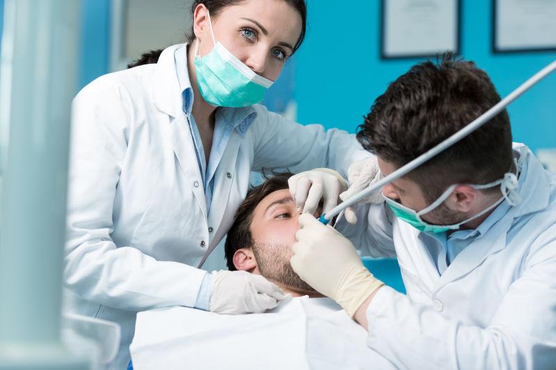 两个牙医正在检查男病人的牙齿