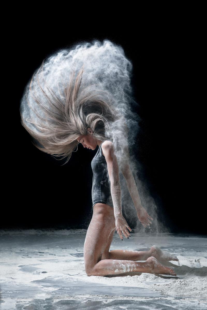 黑色背景下跪在地上使用头发甩出面粉的舞者