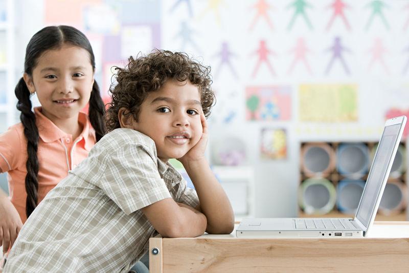 坐在教室内的木桌前使用笔记本电脑的男孩和女孩