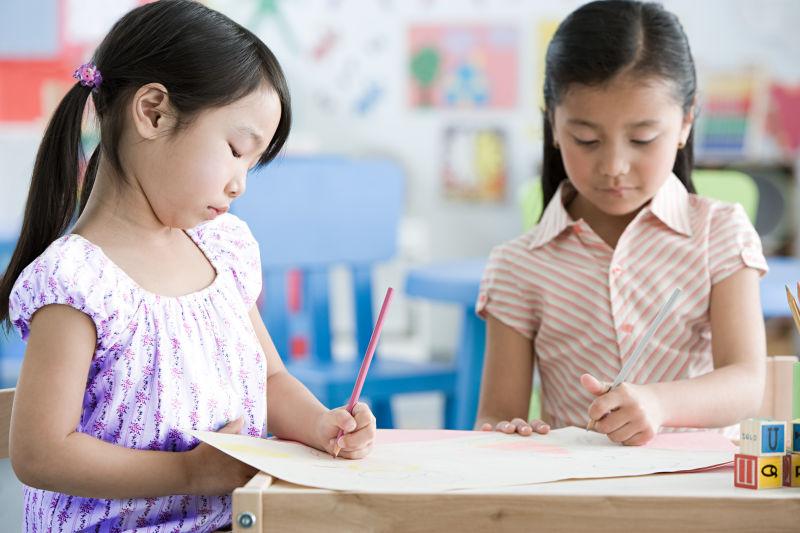 坐在教室的课桌前画画的两个女孩子
