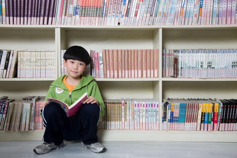 在图书馆内书架旁边看书的男孩