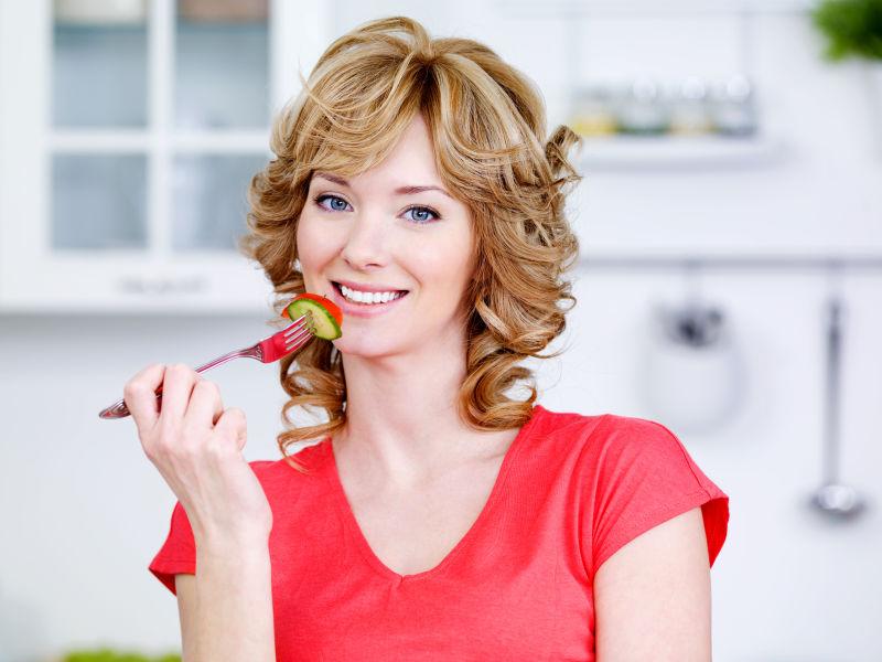 美丽的微笑女人在厨房里吃沙拉的肖像