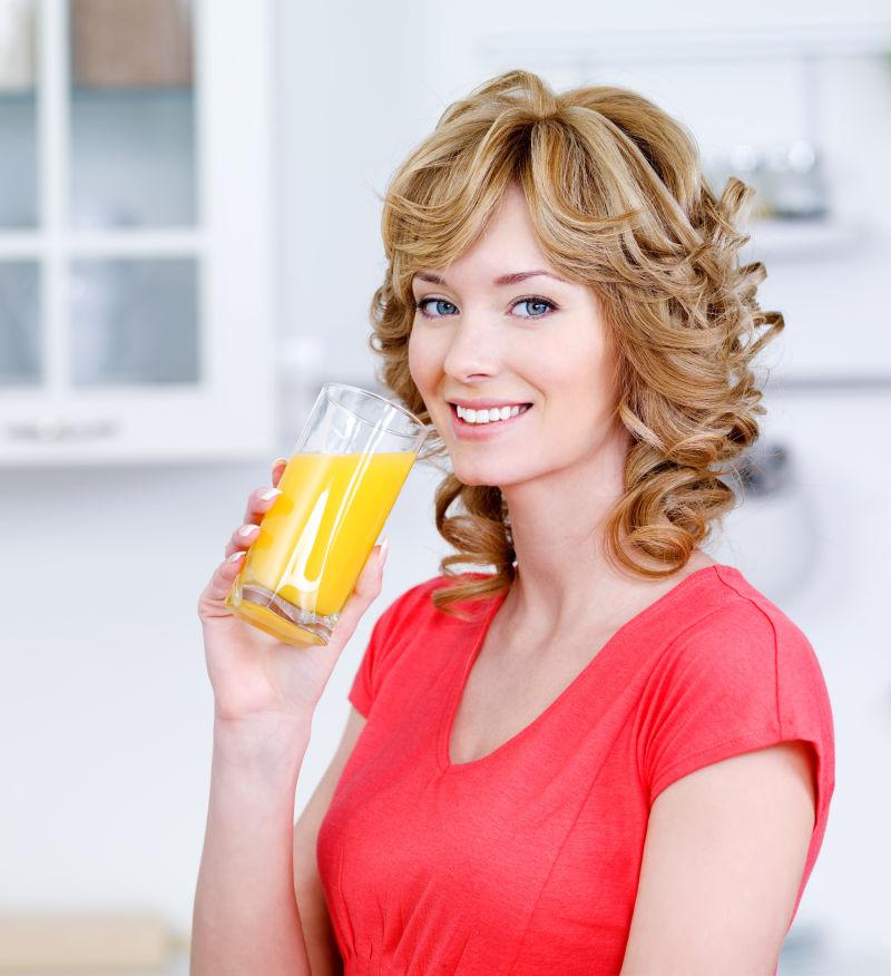 快乐笑容的金发女人在厨房里喝橙汁