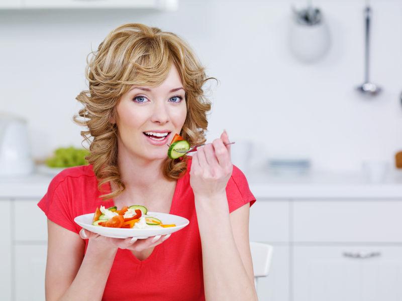 年轻的微笑女人在厨房里吃沙拉