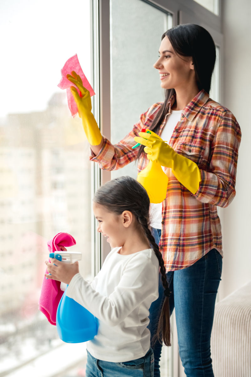 美女和她的女儿微笑着用清洁剂擦窗户