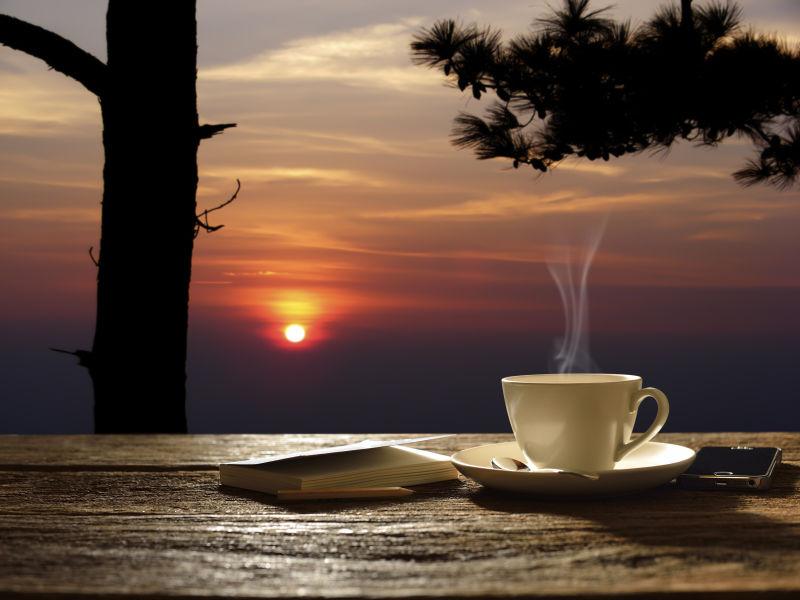 日出背景下木桌上冒着热气的咖啡