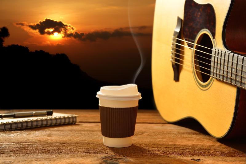 群山上的日出背景下的木桌上吉他旁的一杯热咖啡