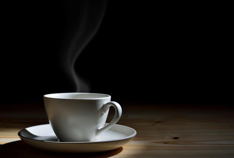 黑色背景下的木桌上的一杯热咖啡