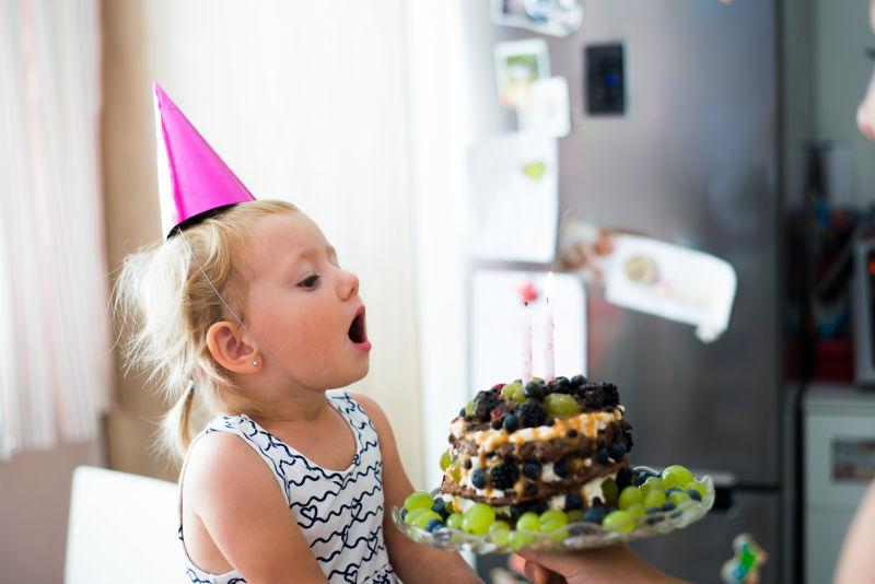 爱的小女孩在她的生日蛋糕上吹蜡烛