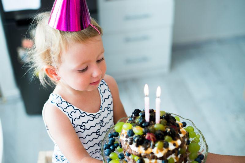 可爱的小女孩带着两个蜡烛的水果生日蛋糕