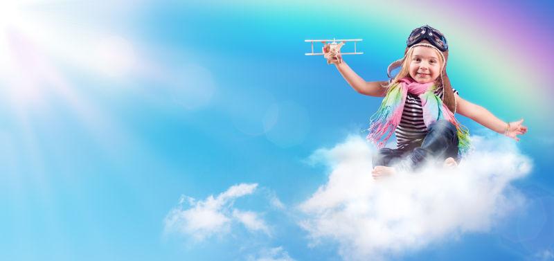 有彩虹的晴天阳光下的云上玩玩具飞机的小女孩