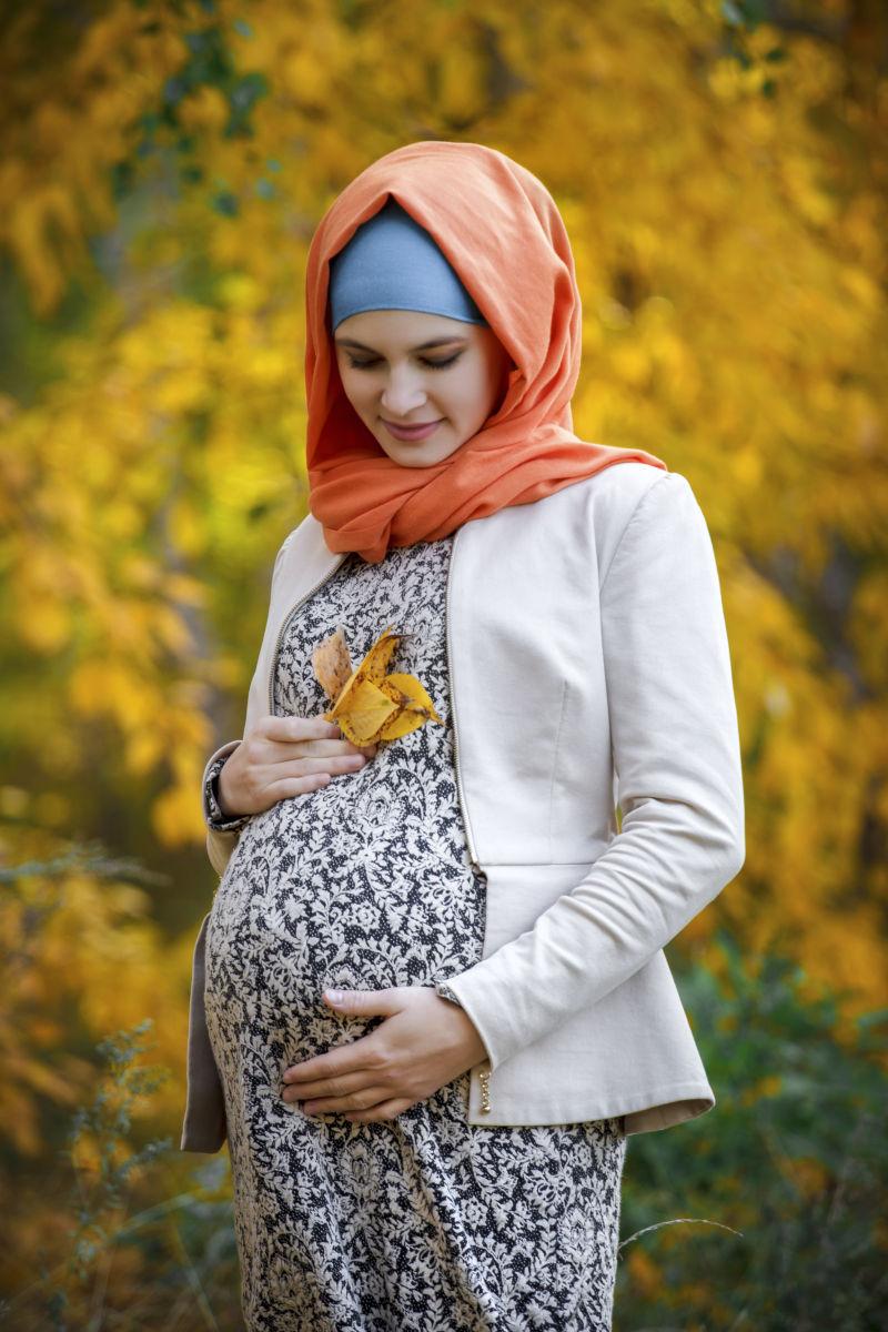 戴着头巾的怀孕的孕妇站在户外
