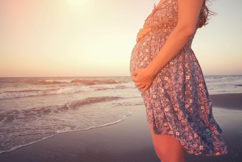 夕阳下站在海滩上的孕妇