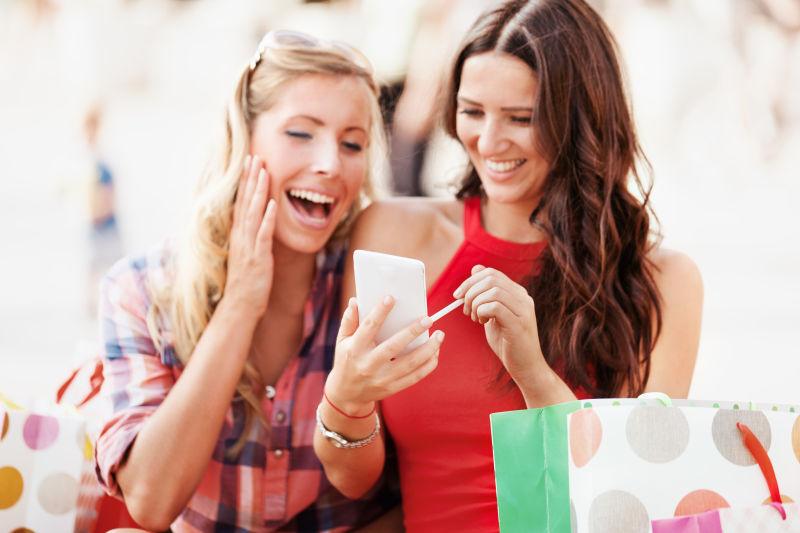 兴奋的拎着购物袋的美女用手机在聊天